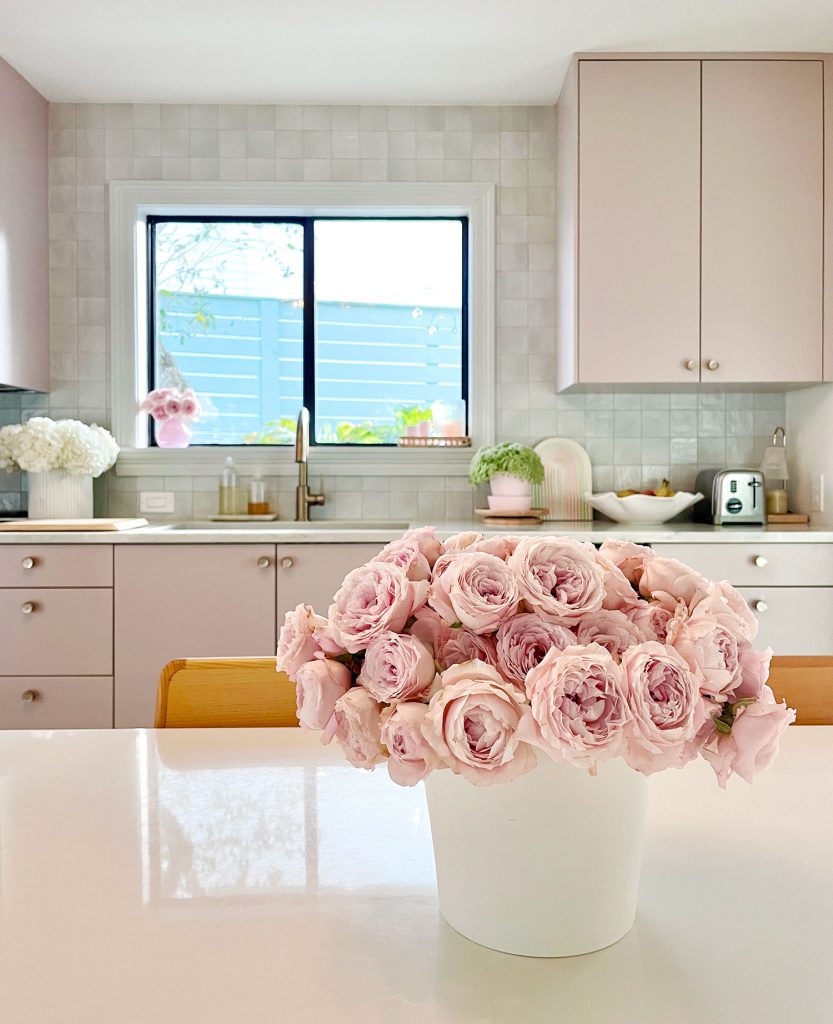 Pink Roses On Breakfast Table In Kitchen With Mauve Cabinets And Tile Backsplash